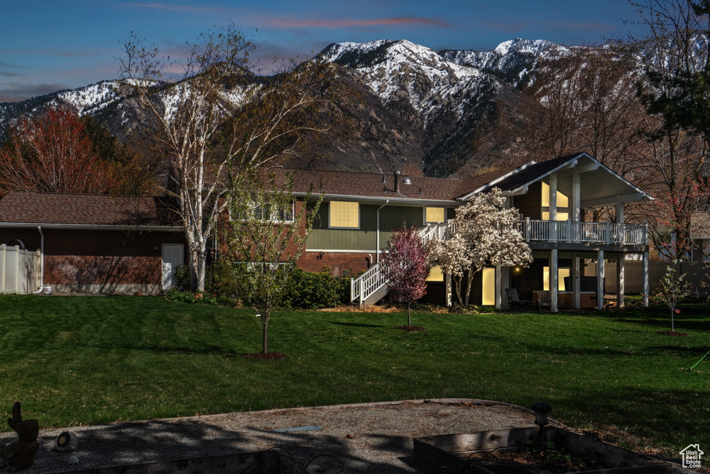 View of front of home with a mountain view, a yard, and a balcony