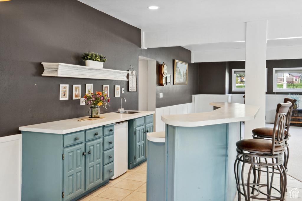 Kitchen featuring a kitchen island, a kitchen breakfast bar, sink, blue cabinets, and light tile floors