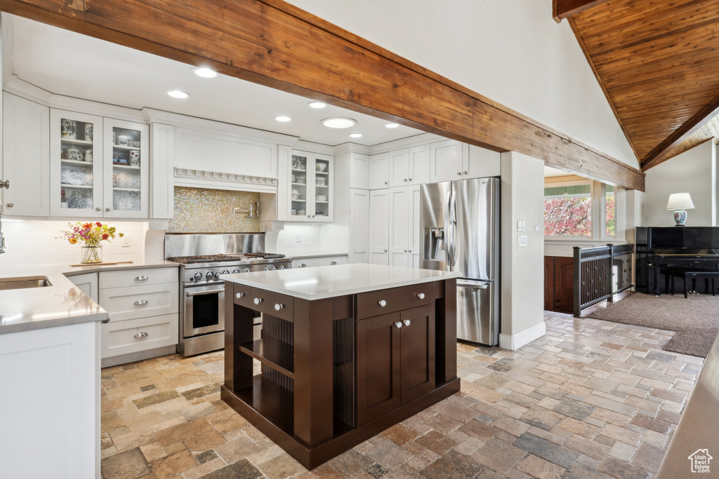 Kitchen featuring appliances with stainless steel finishes, a center island, vaulted ceiling with beams, backsplash, and white cabinetry