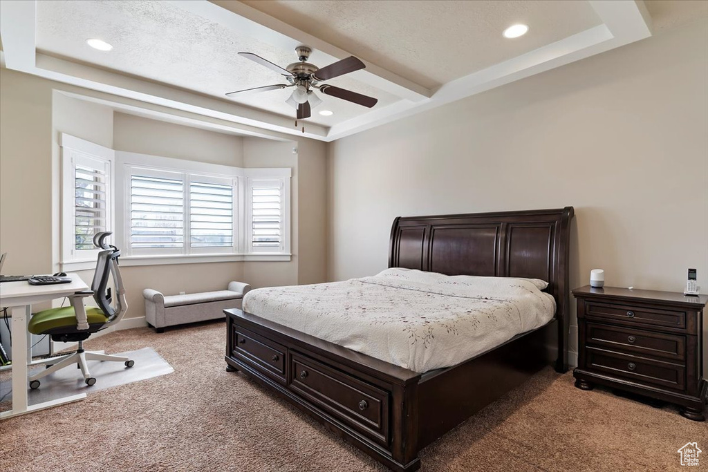 Bedroom with a raised ceiling, ceiling fan, and light carpet