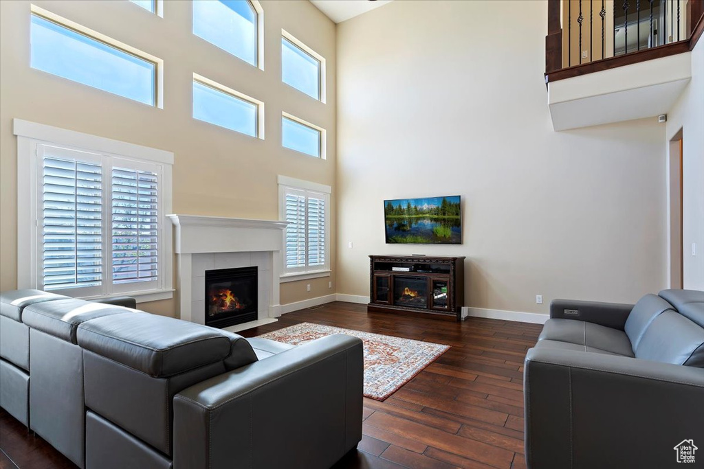 Living room featuring a wealth of natural light, dark wood-type flooring, a high ceiling, and a fireplace