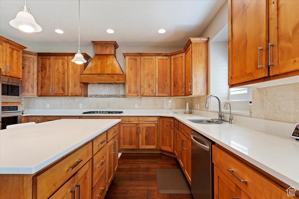 Kitchen featuring decorative light fixtures, stainless steel appliances, custom range hood, dark wood-type flooring, and sink