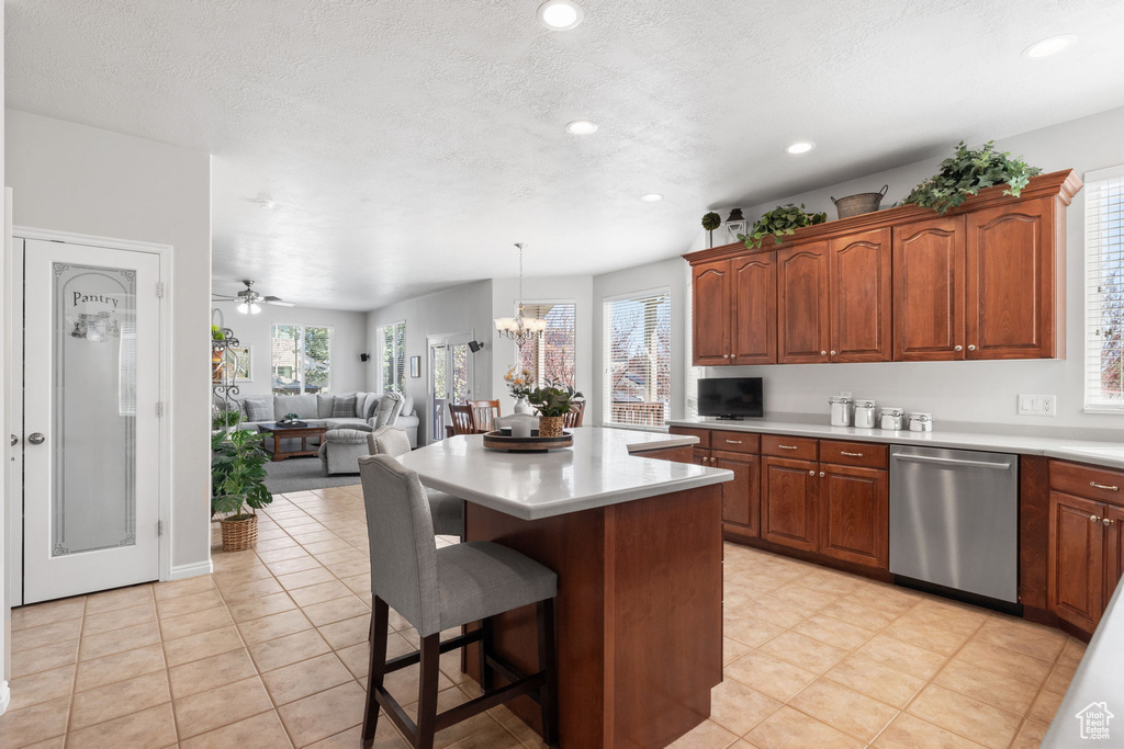Kitchen with a center island, hanging light fixtures, ceiling fan with notable chandelier, light tile floors, and stainless steel dishwasher