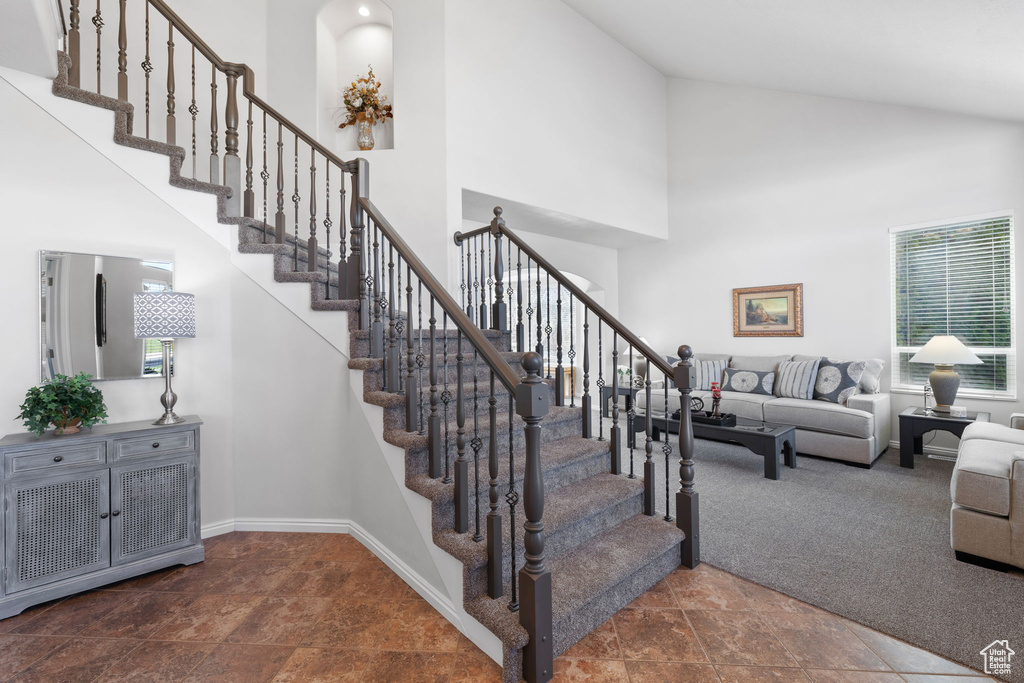 Stairway featuring high vaulted ceiling, a wealth of natural light, and dark colored carpet