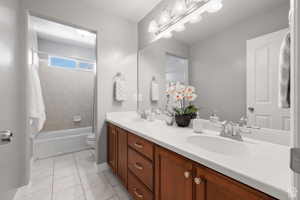 Full bathroom with dual bowl vanity, tiled shower / bath, toilet, and tile flooring
