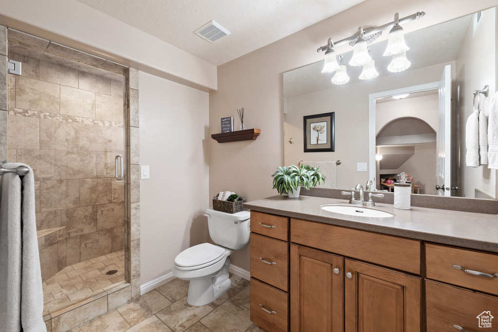 Bathroom with a shower with door, large vanity, toilet, a textured ceiling, and tile floors