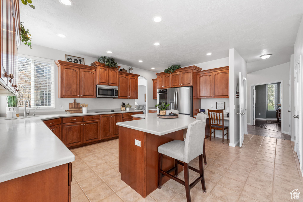 Kitchen featuring a center island, appliances with stainless steel finishes, sink, light tile floors, and a kitchen bar