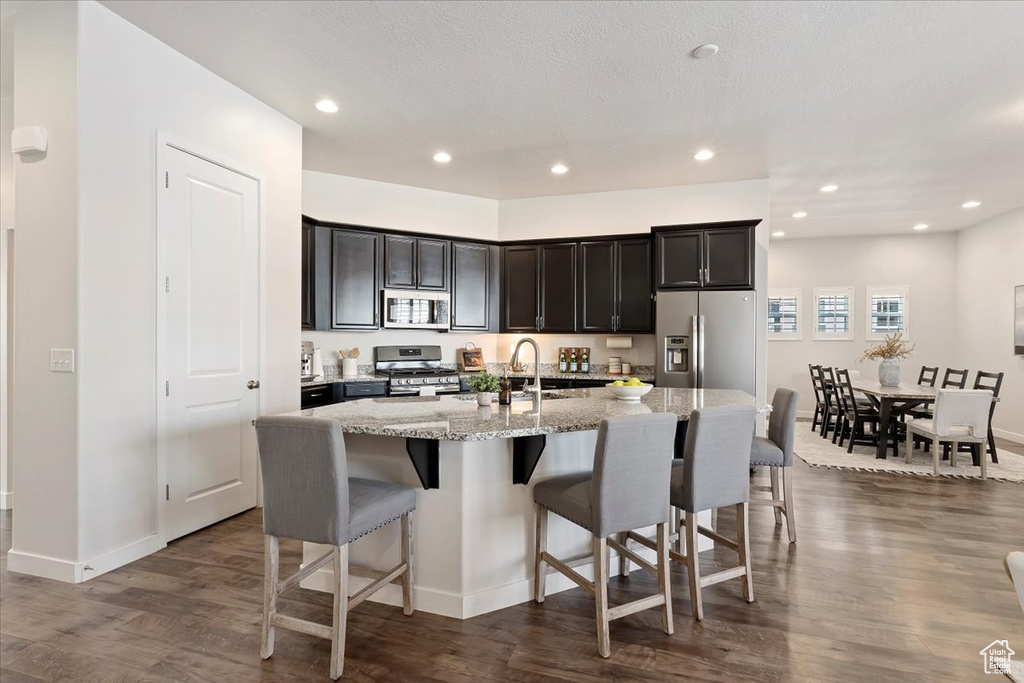 Kitchen with light stone counters, appliances with stainless steel finishes, an island with sink, and dark hardwood / wood-style floors