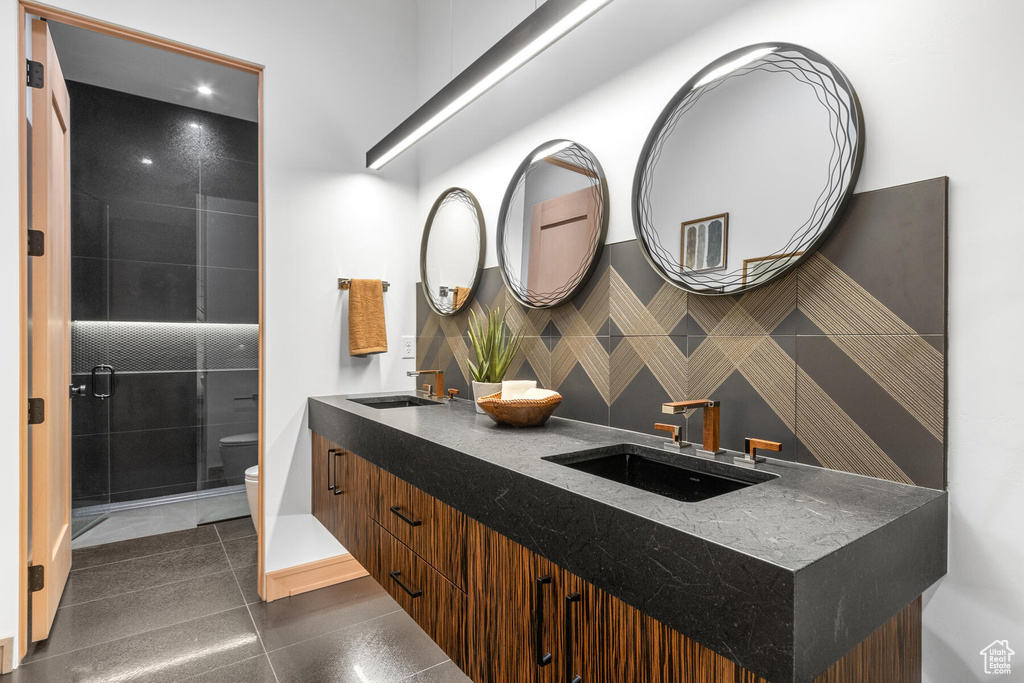Bathroom with vanity with extensive cabinet space, tasteful backsplash, double sink, tile floors, and toilet