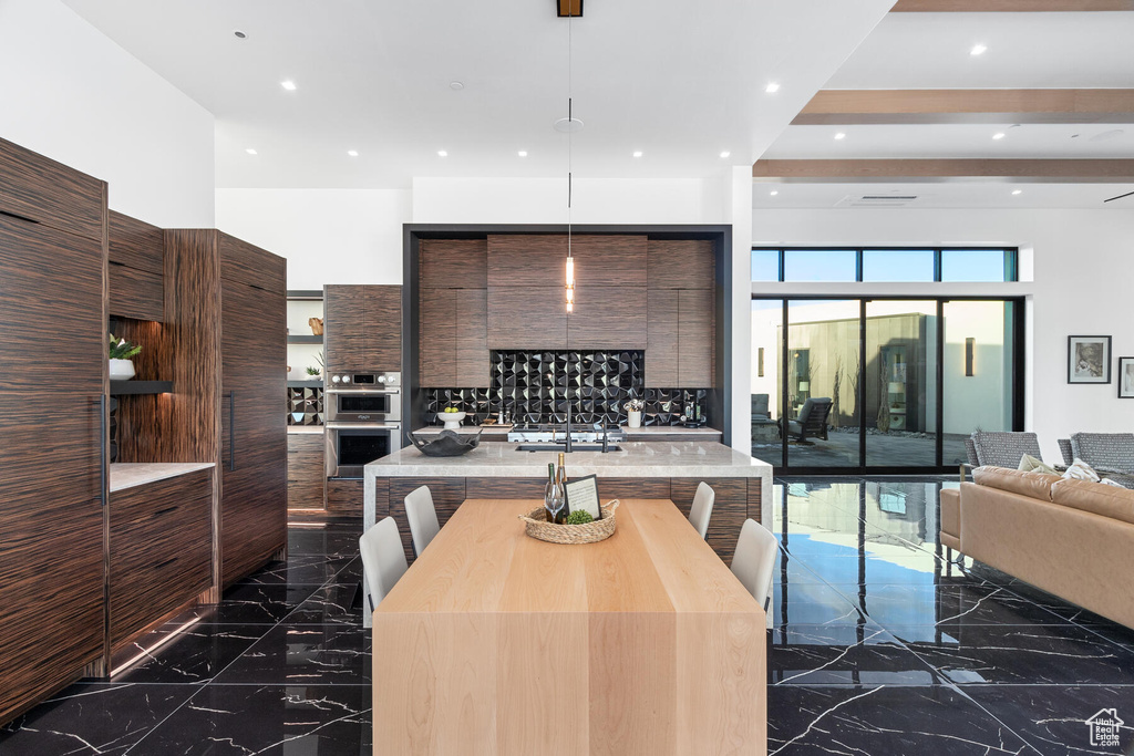 Kitchen with dark brown cabinetry, a breakfast bar, dark tile flooring, stainless steel double oven, and an island with sink
