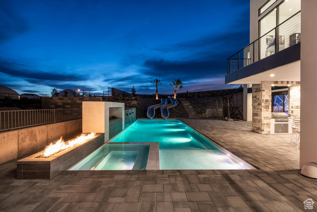 Pool at dusk with a patio area, an in ground hot tub, and a water slide