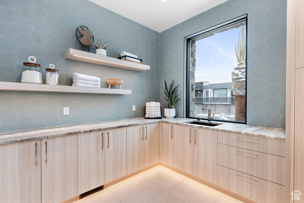 Kitchen with light tile floors, light brown cabinetry, sink, tasteful backsplash, and light stone countertops