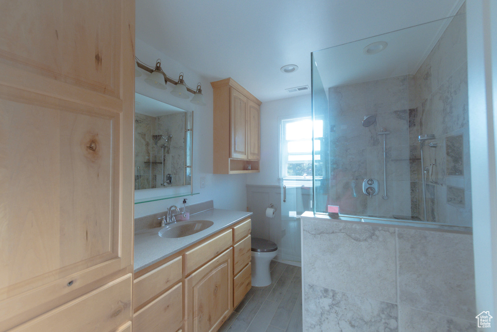 Bathroom with hardwood / wood-style floors, large vanity, a shower with shower door, and toilet
