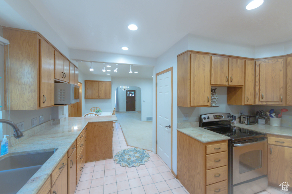 Kitchen with stainless steel electric range oven, sink, light stone countertops, and light tile flooring