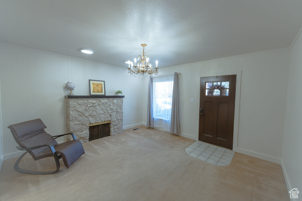 Carpeted foyer entrance featuring ornamental molding, a notable chandelier, and a fireplace