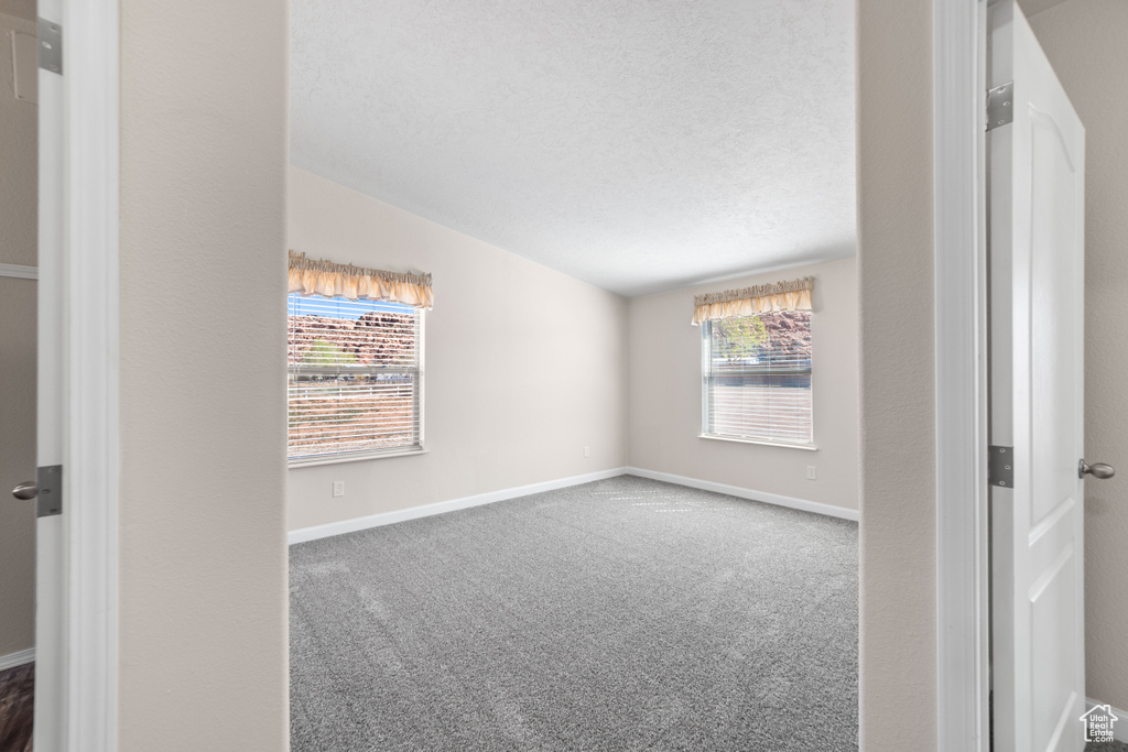 Spare room with lofted ceiling, dark carpet, and a textured ceiling