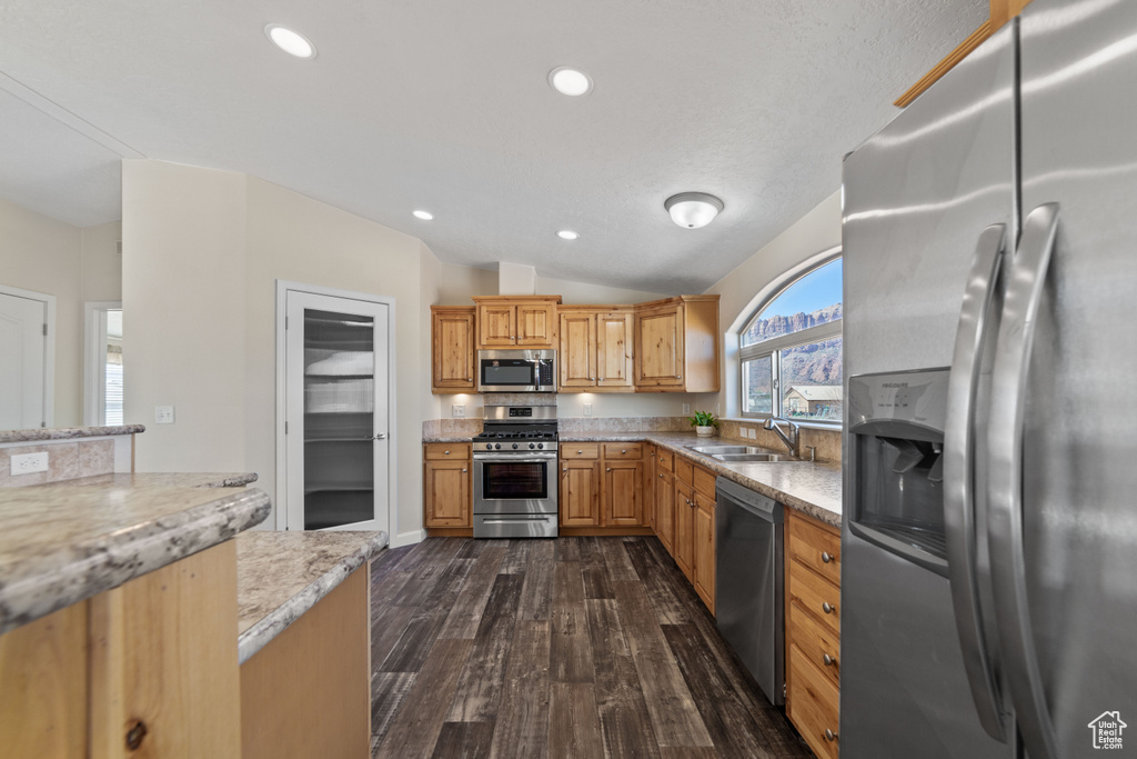 Kitchen with appliances with stainless steel finishes, sink, dark hardwood / wood-style flooring, vaulted ceiling, and light stone countertops