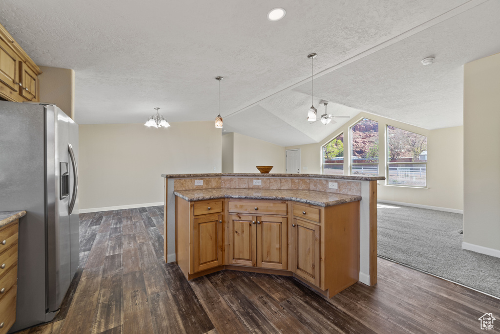 Kitchen featuring decorative light fixtures, dark colored carpet, vaulted ceiling, stainless steel refrigerator with ice dispenser, and light stone countertops