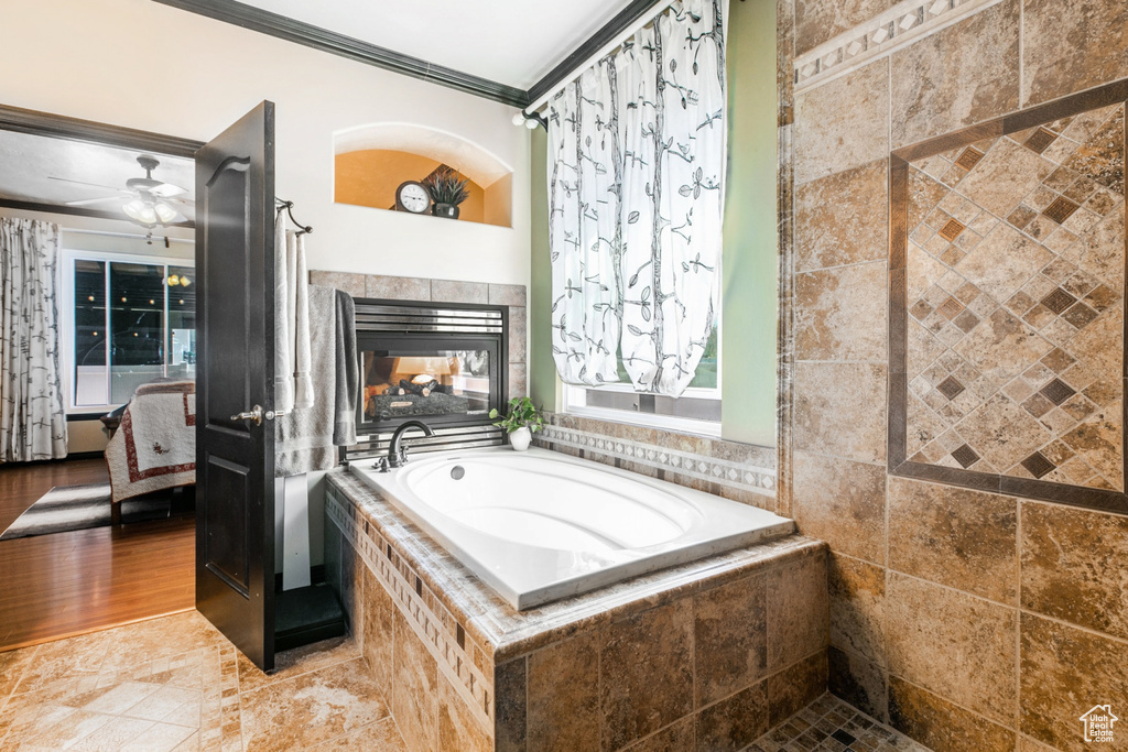Bathroom featuring ceiling fan, crown molding, tile flooring, a tile fireplace, and tiled bath