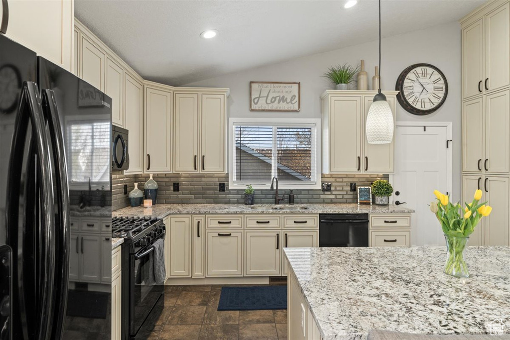 Kitchen with decorative light fixtures, backsplash, vaulted ceiling, black appliances, and sink