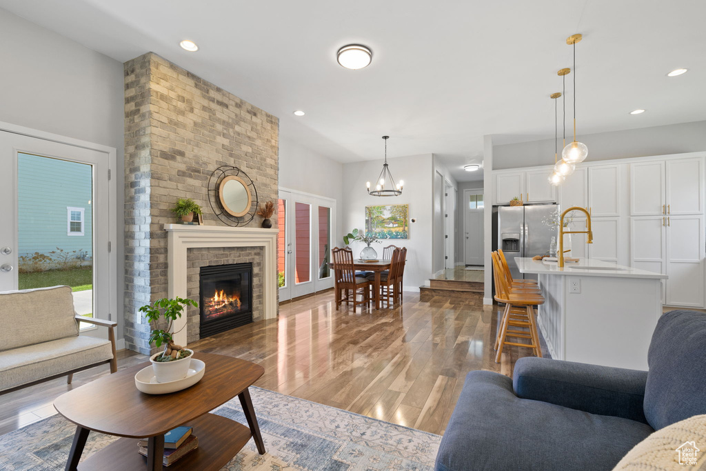 Living room featuring a brick fireplace, brick wall, sink, a notable chandelier, and light wood-type flooring