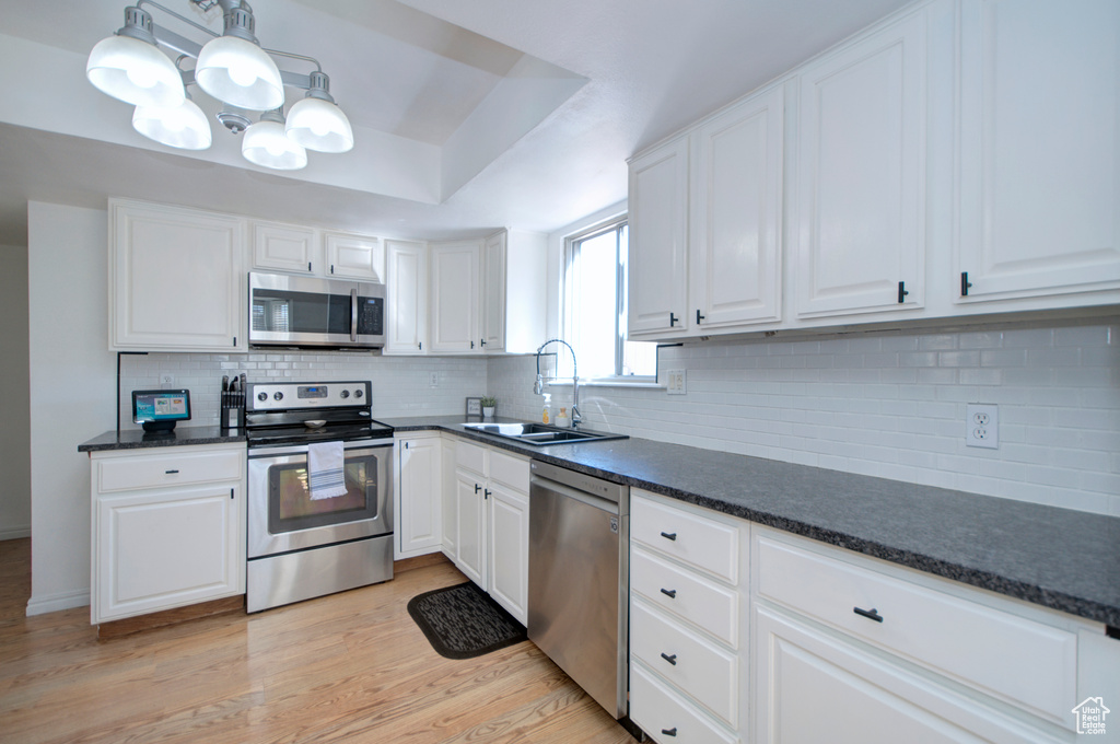 Kitchen featuring stainless steel appliances, white cabinets, decorative light fixtures, and light wood-type flooring