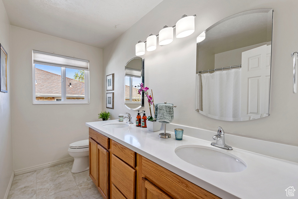 Bathroom featuring tile flooring, toilet, and dual vanity