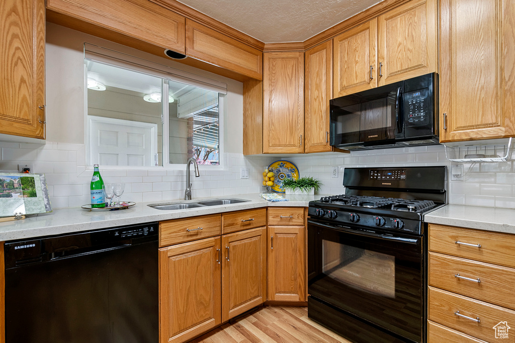 Kitchen with backsplash, light hardwood / wood-style flooring, and black appliances