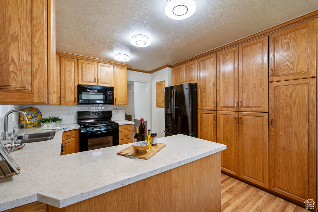 Kitchen featuring backsplash, light hardwood / wood-style flooring, black appliances, light stone counters, and sink