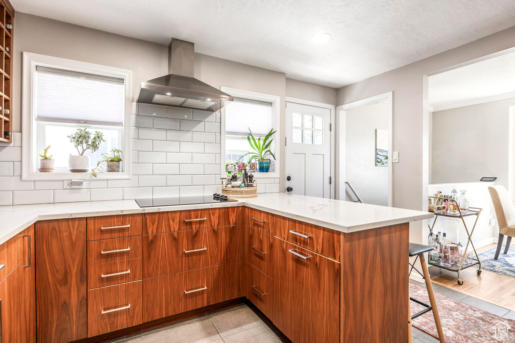 Kitchen with backsplash, kitchen peninsula, wall chimney range hood, and light tile floors