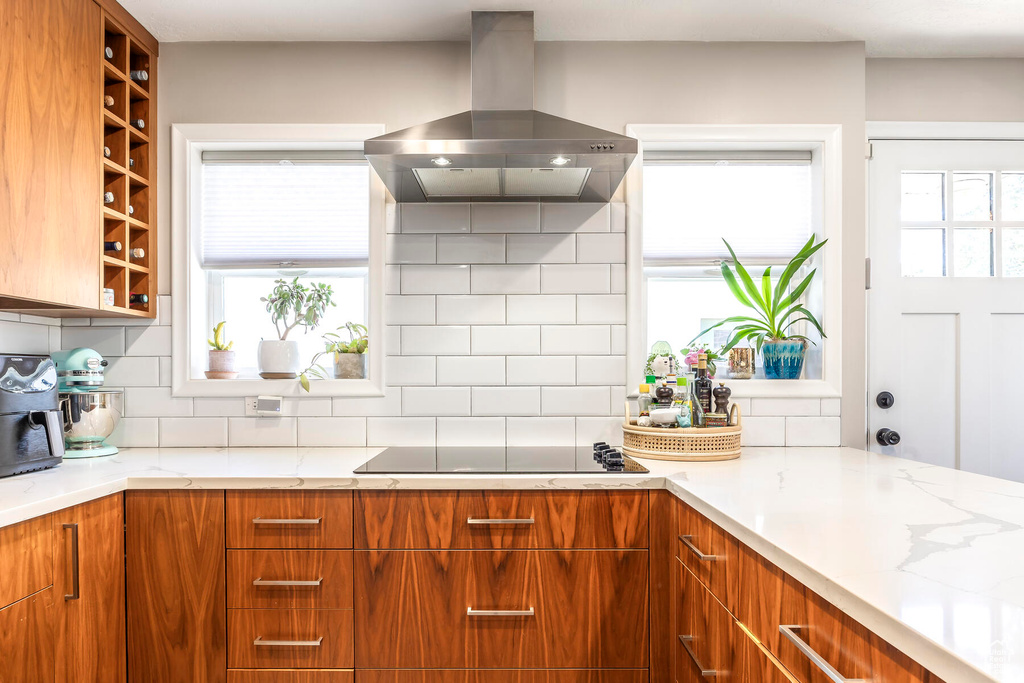 Kitchen featuring a wealth of natural light, tasteful backsplash, island range hood, and black electric stovetop