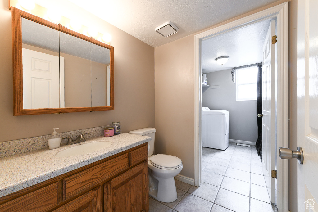 Bathroom with washer / dryer, toilet, a textured ceiling, vanity, and tile floors