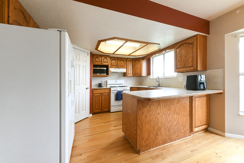 Kitchen featuring sink, white appliances, kitchen peninsula, and light hardwood / wood-style flooring