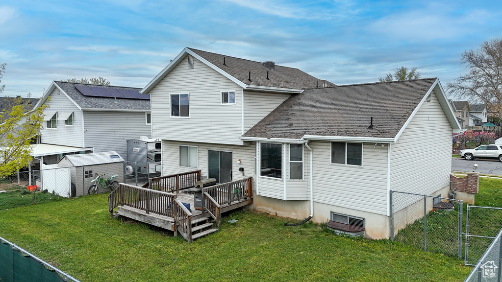 Back of property featuring solar panels, a wooden deck, a storage unit, and a lawn