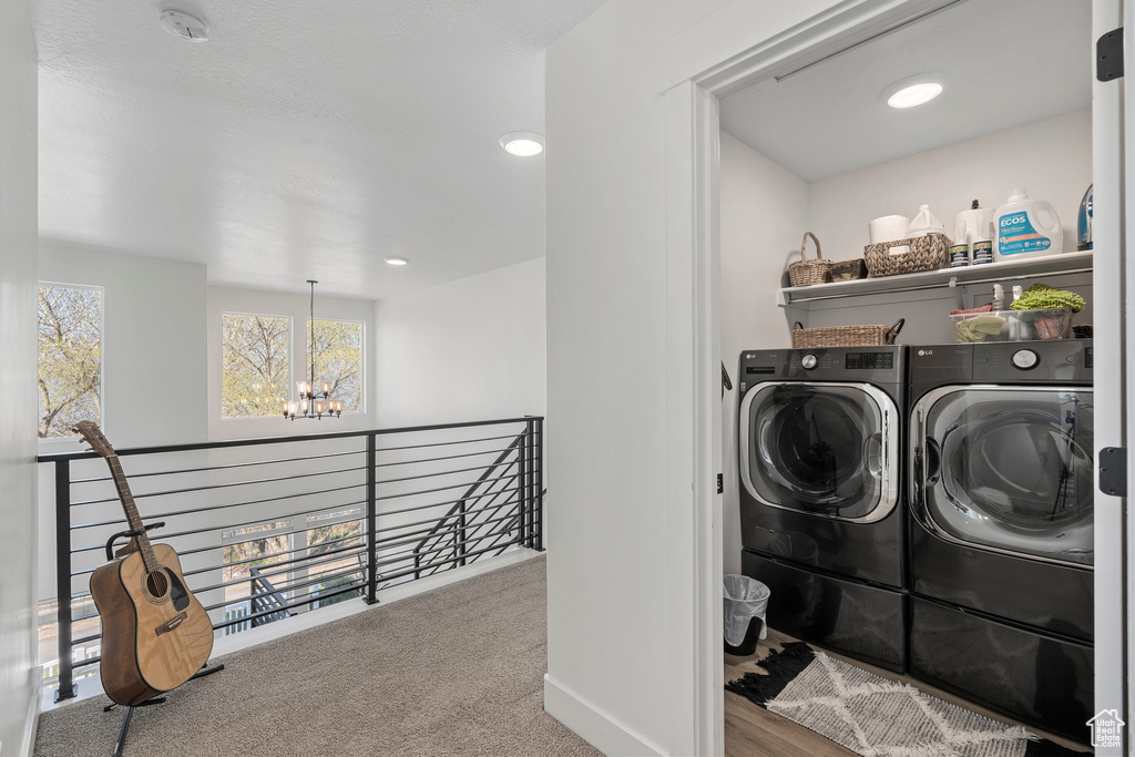 Washroom featuring light colored carpet, washer and clothes dryer, and an inviting chandelier