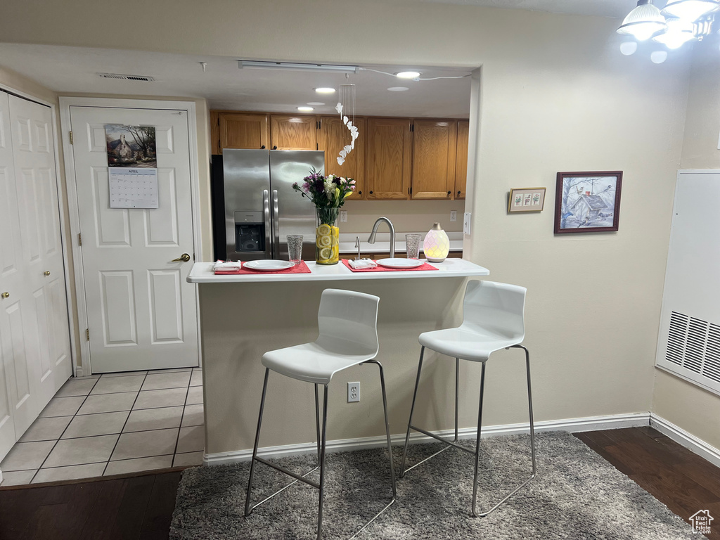 Kitchen featuring hanging light fixtures, a breakfast bar, stainless steel refrigerator with ice dispenser, sink, and light tile floors
