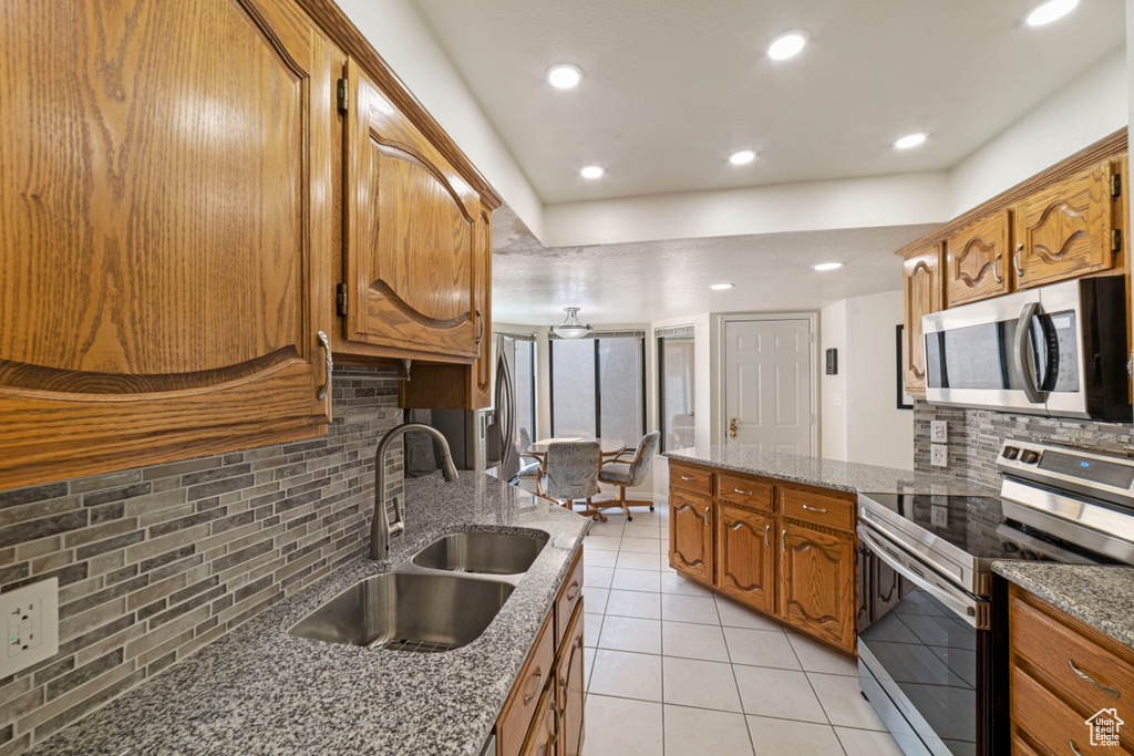 Kitchen with appliances with stainless steel finishes, sink, backsplash, light tile flooring, and light stone countertops