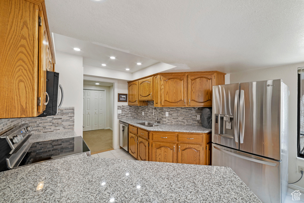 Kitchen featuring light stone countertops, appliances with stainless steel finishes, backsplash, sink, and light tile floors