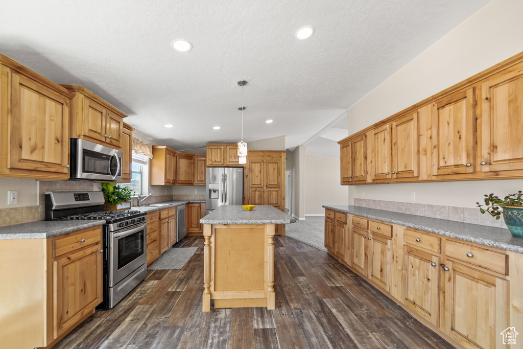 Kitchen featuring pendant lighting, dark hardwood / wood-style floors, appliances with stainless steel finishes, a kitchen bar, and a kitchen island