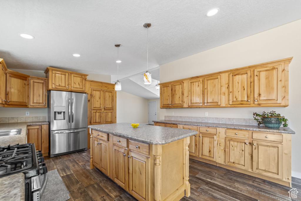Kitchen with appliances with stainless steel finishes, hanging light fixtures, vaulted ceiling, dark wood-type flooring, and a center island