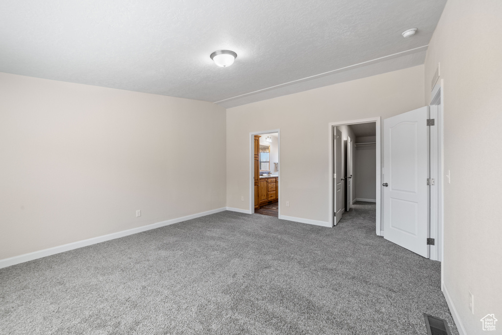Unfurnished bedroom with a spacious closet, connected bathroom, and dark carpet