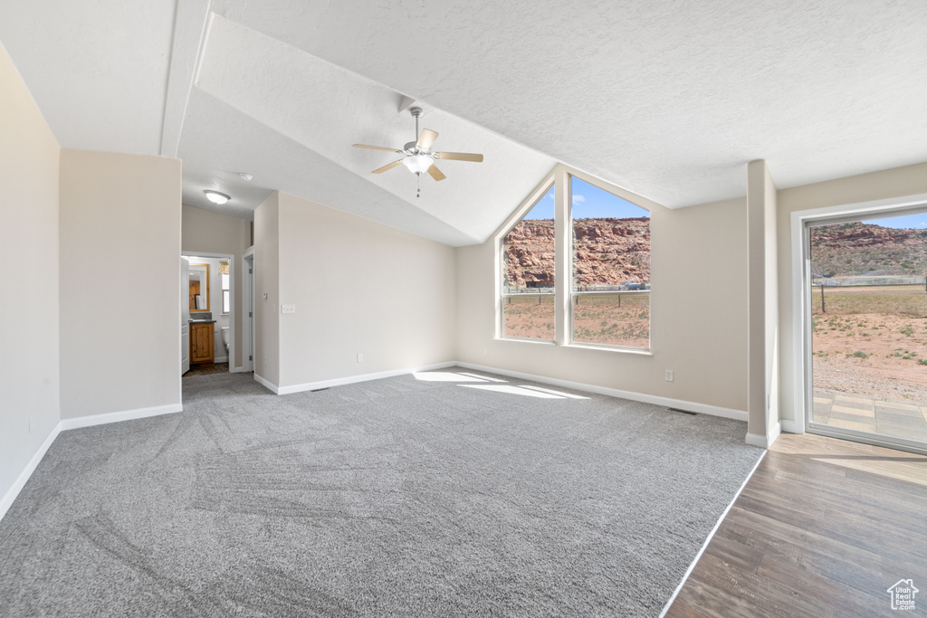 Unfurnished living room with light colored carpet, ceiling fan, a textured ceiling, and lofted ceiling