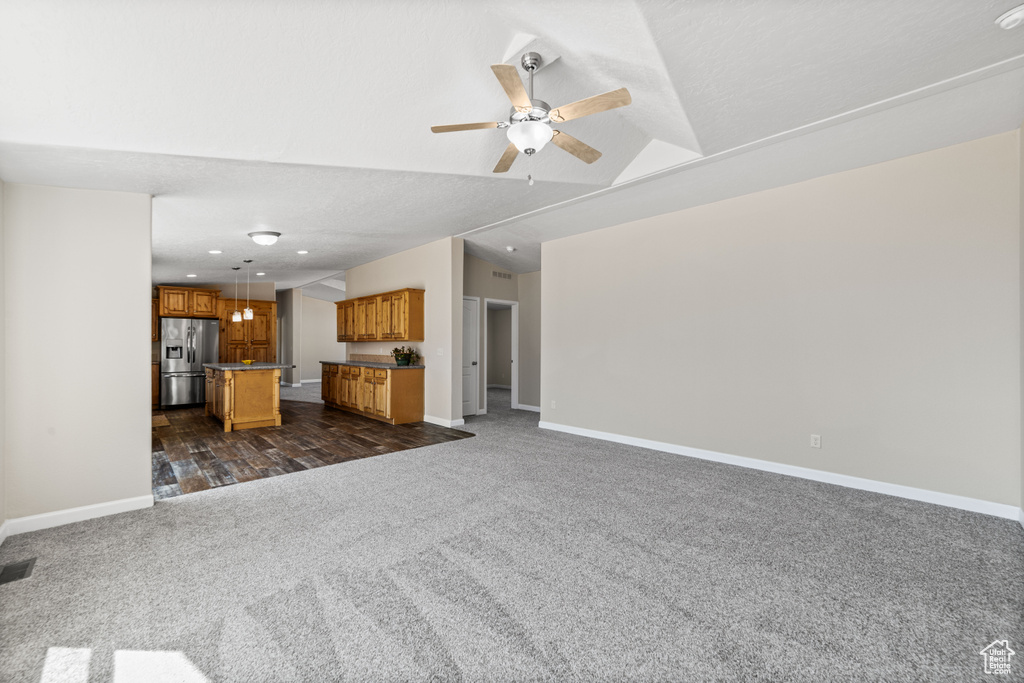 Unfurnished living room featuring vaulted ceiling, ceiling fan, and dark colored carpet