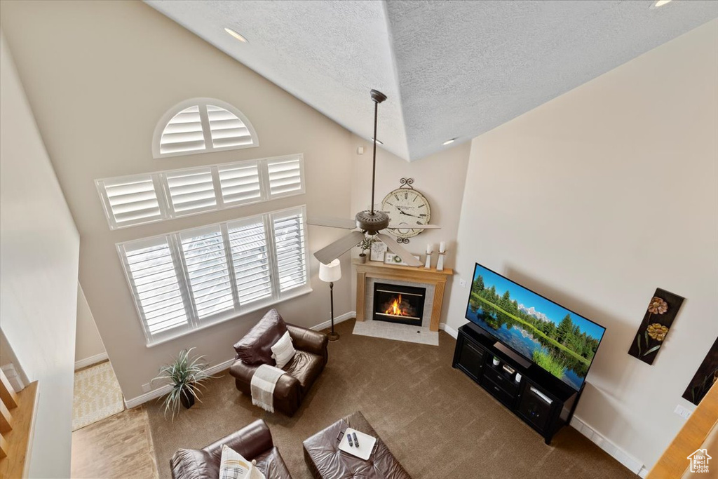 Living room featuring ceiling fan, a textured ceiling, high vaulted ceiling, and dark carpet