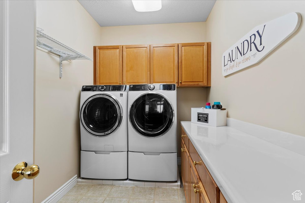 Laundry area featuring washing machine and dryer, light tile flooring, and cabinets