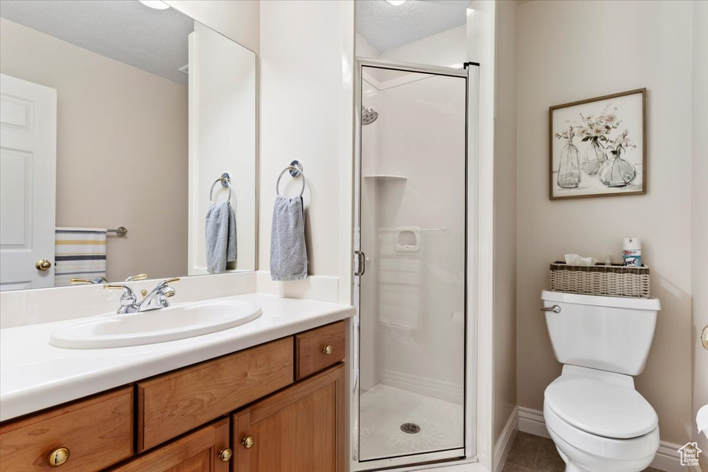 Bathroom with tile flooring, a textured ceiling, toilet, a shower with shower door, and vanity
