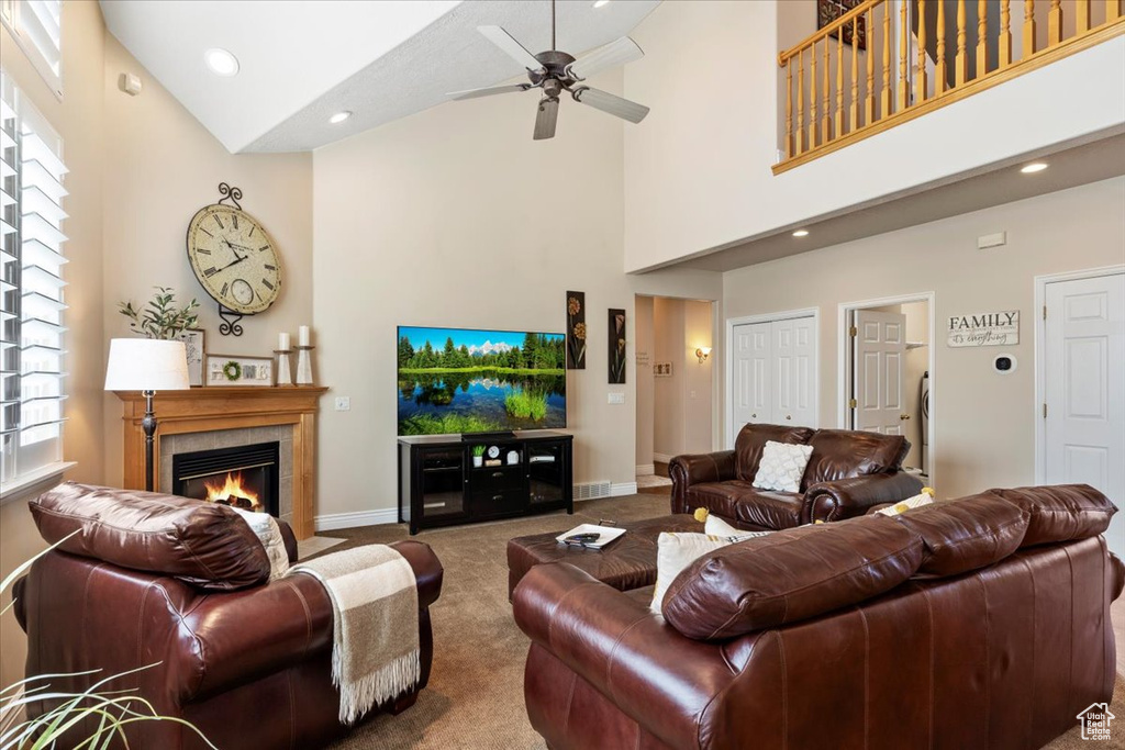 Living room with high vaulted ceiling, ceiling fan, a tile fireplace, and dark colored carpet