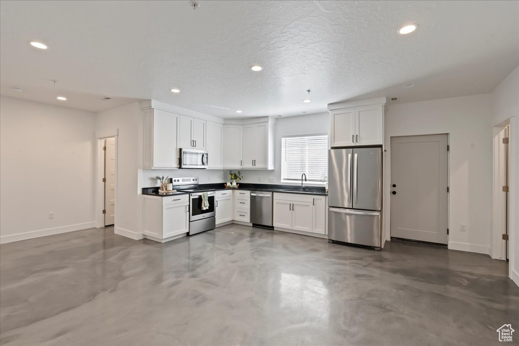 Kitchen with concrete flooring, stainless steel appliances, white cabinets, and a textured ceiling