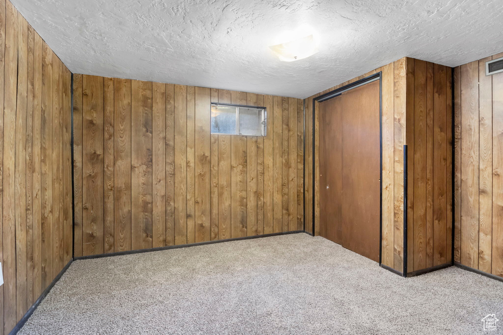 Carpeted spare room featuring wood walls and a textured ceiling