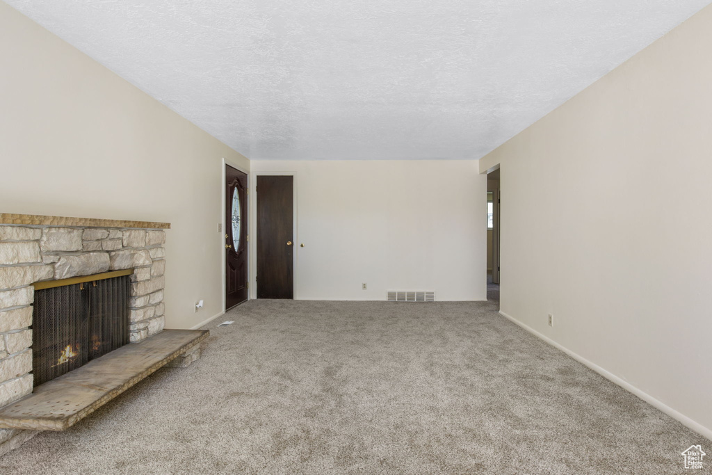 Unfurnished living room featuring light carpet, a fireplace, and a textured ceiling
